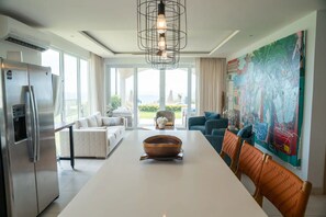 A modern kitchen with a stainless steel refrigerator, a dining table with a copper bowl centerpiece, and a large window offering a view of the outdoors. - Beautiful Ground Floor Condo with Spectacular Ocean Views and Resort Style Amenities (Playa Tamarindo, Guanacaste Province)