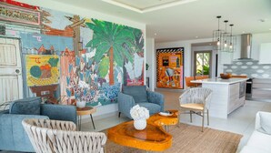 Uma sala de estar moderna com um grande mural abstrato, uma cozinha com ilha central e uma área de jantar com vista para o exterior.