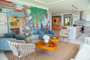 Ein modernes Wohnzimmer mit einer großen abstrakten Wandmalerei, eine Küche mit Kochinsel und ein Essbereich mit Blick ins Freie.