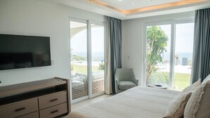 Quarto com cama grande, televisão de tela plana, cômoda e vista para o exterior por grandes janelas.