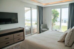 Ein Schlafzimmer mit einem großen Bett, einem Flachbildfernseher, einer Kommode und Blick ins Freie durch große Fenster.