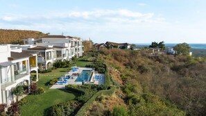 A resort with multiple white buildings, a swimming pool with lounge chairs, and a view of the ocean. - Beautiful Ground Floor Condo with Spectacular Ocean Views and Resort Style Amenities (Playa Tamarindo, Guanacaste Province)