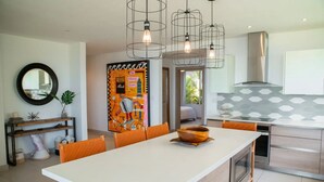 Uma cozinha moderna com ilha central, iluminação pendente e uma obra de arte abstrata colorida.