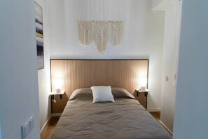 A bedroom with a bed, two bedside tables, a wall-mounted macrame piece, and a framed picture on the wall. - Suite 1 Apartment, Teatro24 (Alicante)