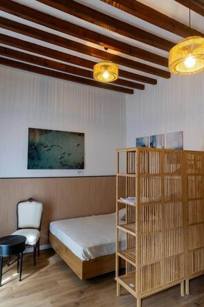 Ein Zimmer mit einem Bett, einem Sessel, einer Holzregaleinheit und einem Bild an der Wand.