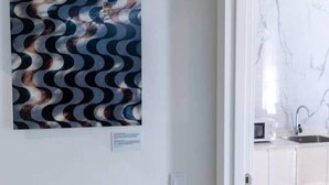 Een kamer met een witte muur, een deur naar een keuken en een lijst met abstracte kunst.