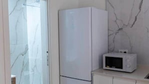 Een compacte keuken met een koelkast, magnetron en een deur naar een badkamer met een douchecabine.