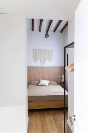 A bedroom with a wooden bed frame, a headboard, a wall-mounted light fixture, and a hanging macrame piece. - Suite 3 Apartment, Teatro24 (Alicante)