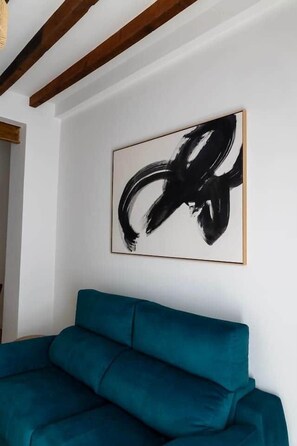 A teal sofa, a black abstract painting, and exposed wooden beams on a white wall. - Suite 3 Apartment, Teatro24 (Alicante)