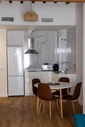 A modern kitchen with white cabinets, a built-in oven, a microwave, and a stove. There is a dining area with a round table and four chairs. - Suite 3 Apartment, Teatro24 (Alicante)