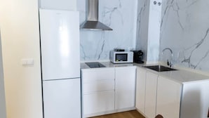 Una cucina compatta con mobili bianchi, forno a microonde integrato, macchina per il caffè e cappa aspirante in acciaio inossidabile.