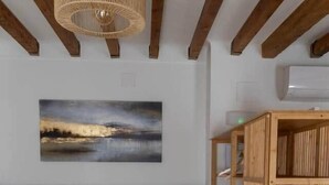 Een slaapkamer met een bed, houten hoofdeinde, een wandlamp, een houten plankunit en een schilderij van een landschap.