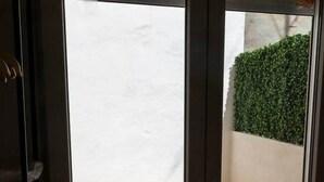 A room with a sliding glass door leading to an outdoor area with a wooden floor and a green hedge. - Suite 5 Apartment, 24 Teatro (Alicante)