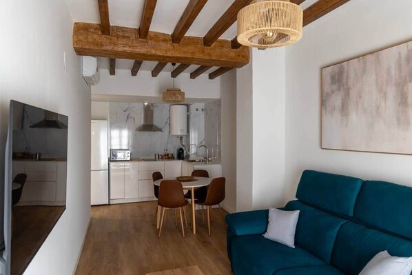 A modern kitchen with white cabinets, a dining area with a table and chairs, and a teal sofa in a living area. - Suite 5 Apartment, 24 Teatro (Alicante)