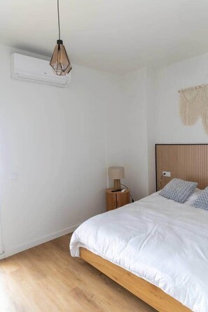 A bedroom with a bed, a hanging light fixture, a bedside table with a lamp, and a wall-mounted air conditioner. - Suite 5 Apartment, 24 Teatro (Alicante)