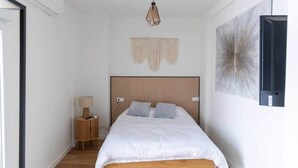 A bedroom with a wooden bed, a bedside table with a lamp, a wall-mounted air conditioner, and a large abstract painting. - Suite 5 Apartment, 24 Teatro (Alicante)
