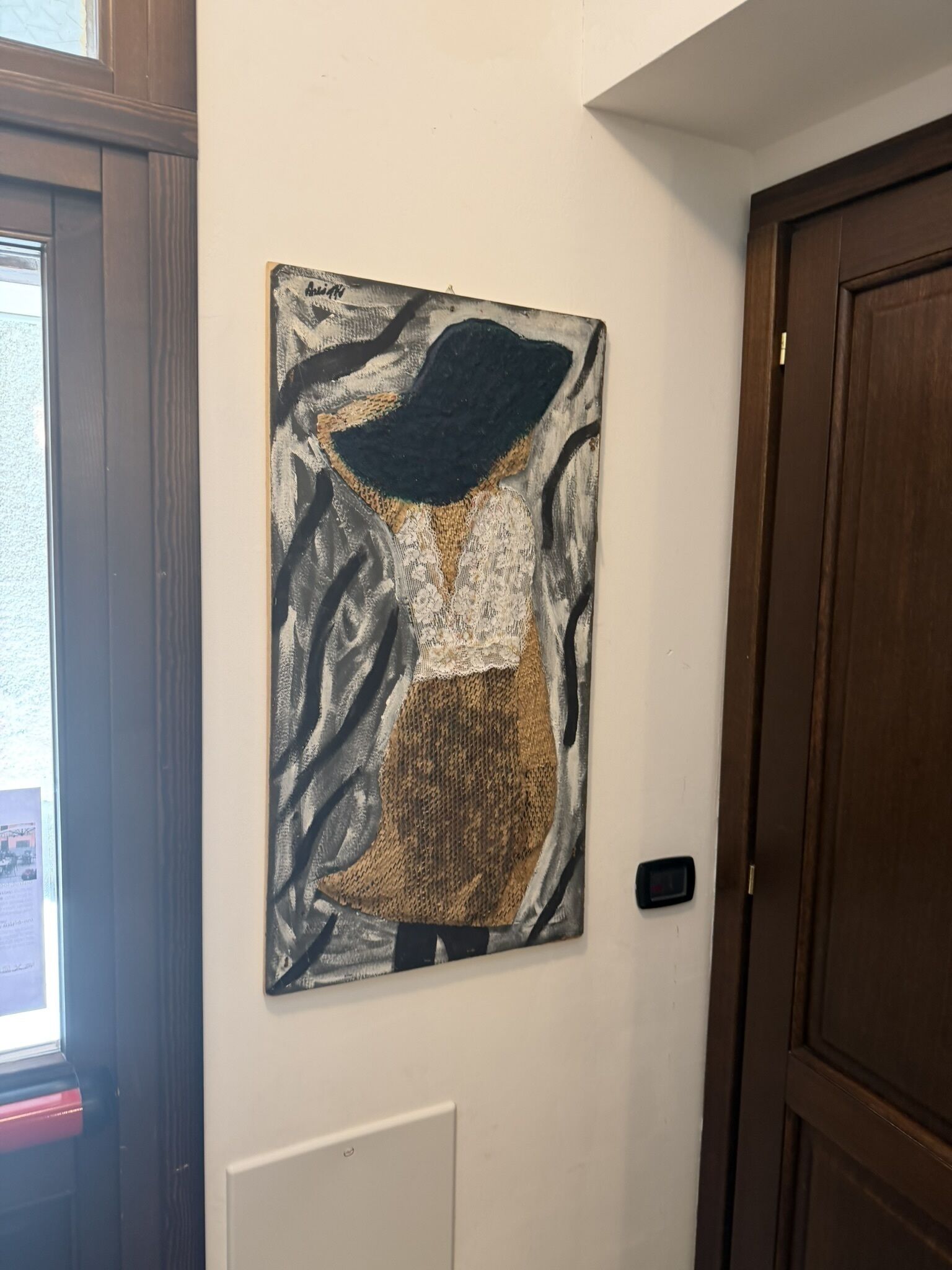 A wall-mounted artwork depicting a figure in a hat and patterned dress.