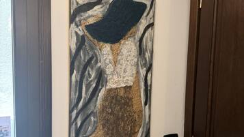 A wall-mounted artwork depicting a figure in a hat and patterned dress.