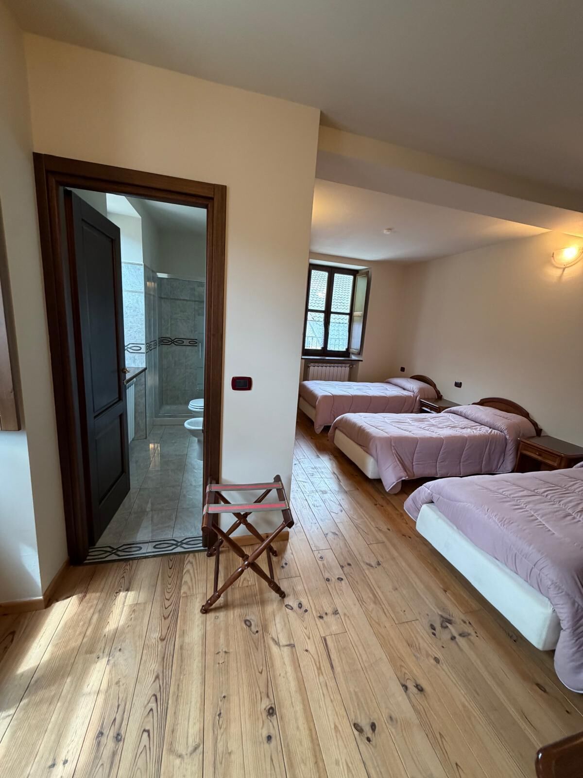 A bedroom with two beds, a wooden floor, a small table, and a window.