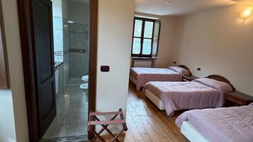 A bedroom with two beds, a wooden floor, a small table, and a window.