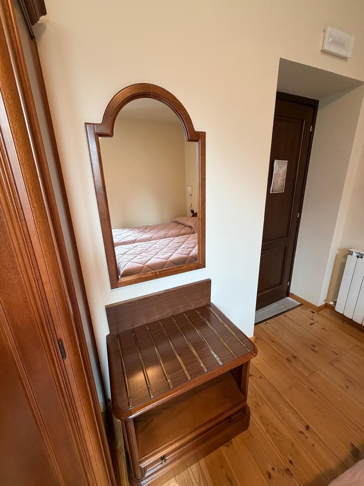 A bedroom with a wooden bed frame, a mirror, and a small wooden shelf.