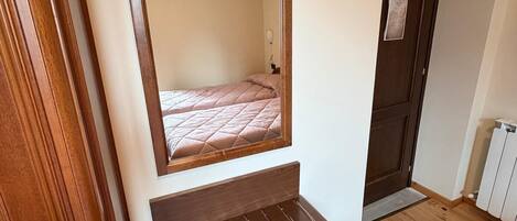 A bedroom with a wooden bed frame, a mirror, and a small wooden shelf.