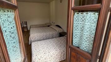 Een kleine kamer met twee bedden, houten vloeren en een deur met een gordijn met patroon.