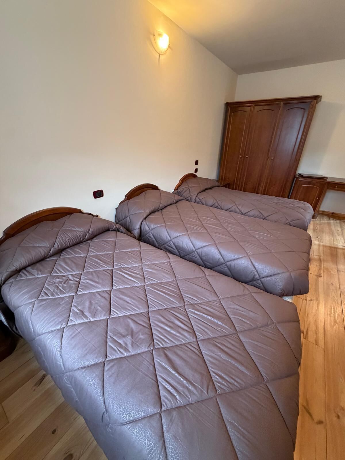 Un dormitorio con dos camas, un armario de madera y una lámpara de pared.