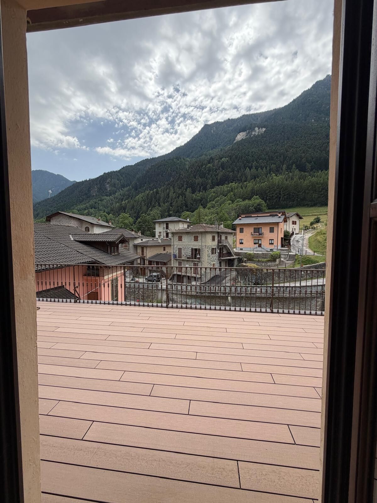 Blick von einem Balkon mit Pflasterboden auf ein Dorf mit traditionellen Gebäuden und einem Berg im Hintergrund.