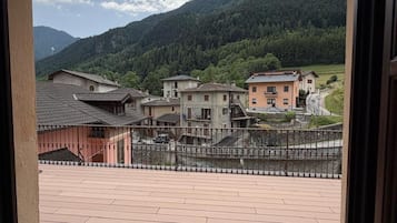 Blick von einem Balkon mit Pflasterboden auf ein Dorf mit traditionellen Gebäuden und einem Berg im Hintergrund.
