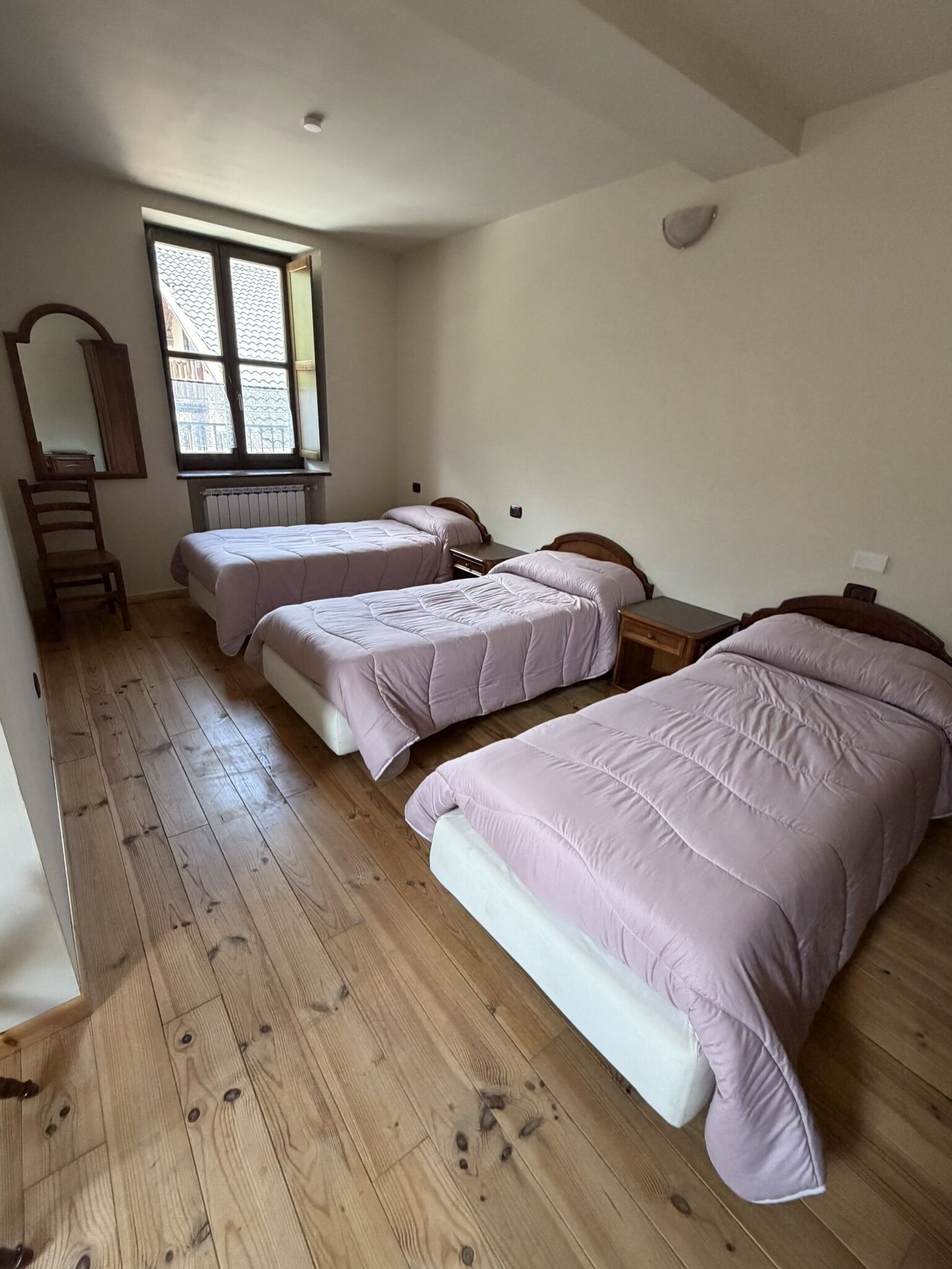 A bedroom with two single beds, a wooden floor, a window with a view, and a radiator.