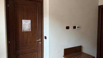 Una habitación con una puerta de madera, un pequeño banco de madera y un termostato en la pared.