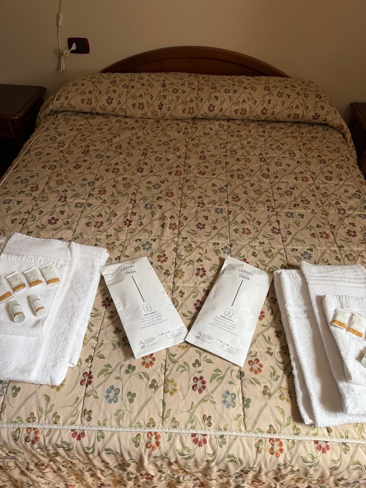 Una cama con una colcha de estampado floral, dos toallas y dos paquetes etiquetados 'Luxury Touch'.