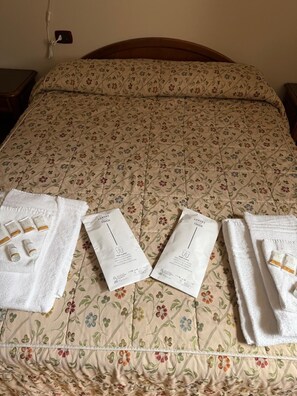 Una cama con una colcha de estampado floral, dos toallas y dos paquetes etiquetados 'Luxury Touch'.