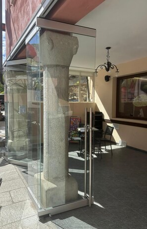 Un edificio moderno con cerramiento de vidrio, una columna de piedra y un comedor con sillas y mesas.