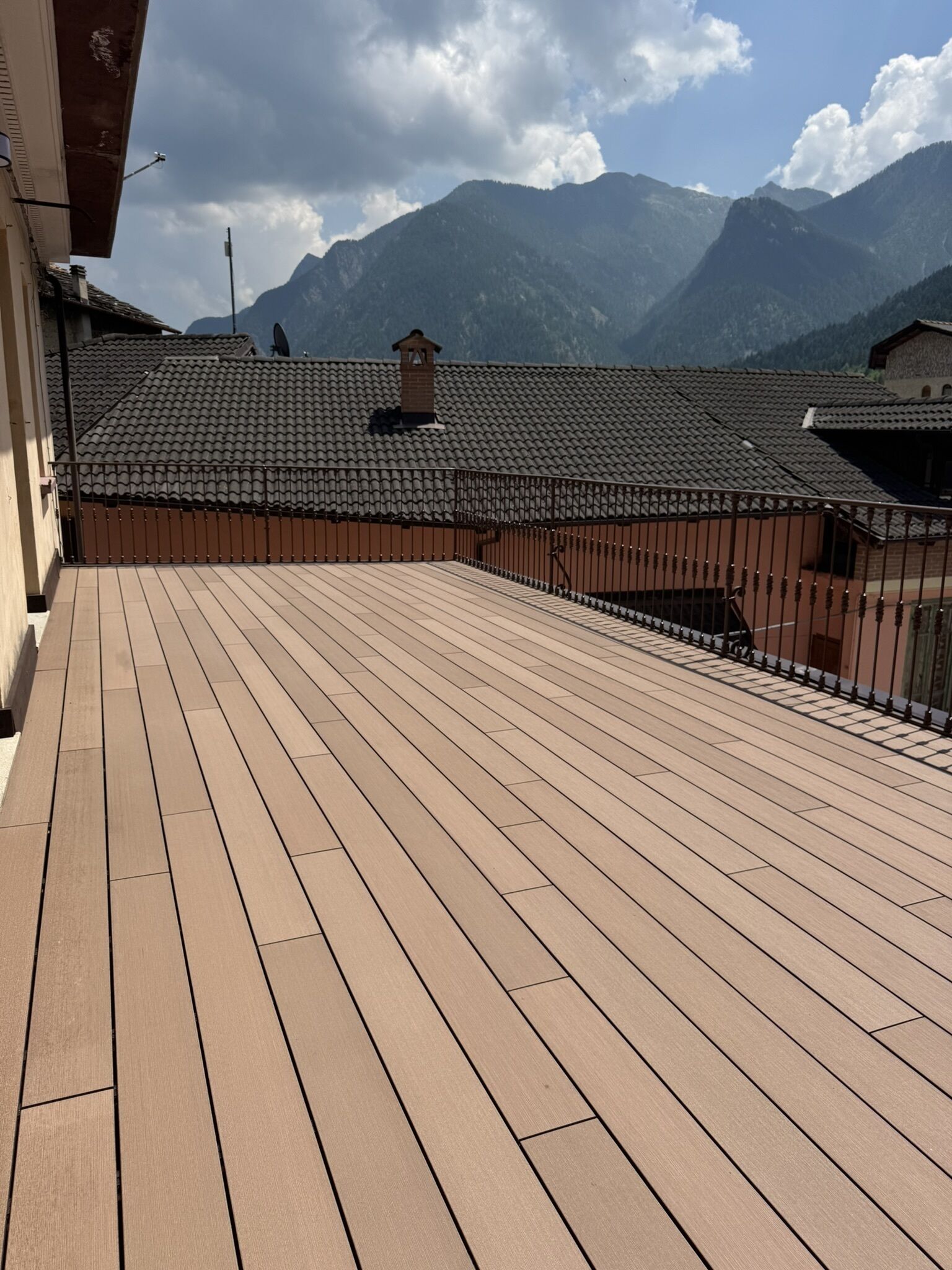 A wooden deck with a metal railing, overlooking a mountainous landscape.