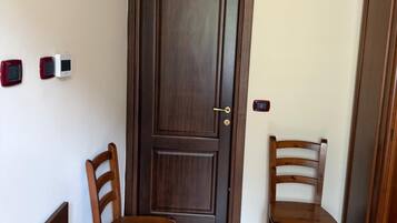 Une pièce avec une porte en bois, deux chaises en bois, une table en bois et un lit recouvert d’une courtepointe à motifs floraux.
