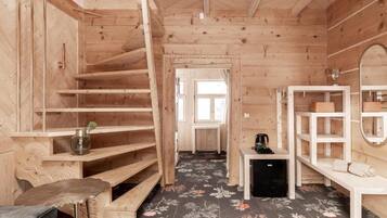 A wooden interior with a staircase, a small table with a kettle, and a bench.