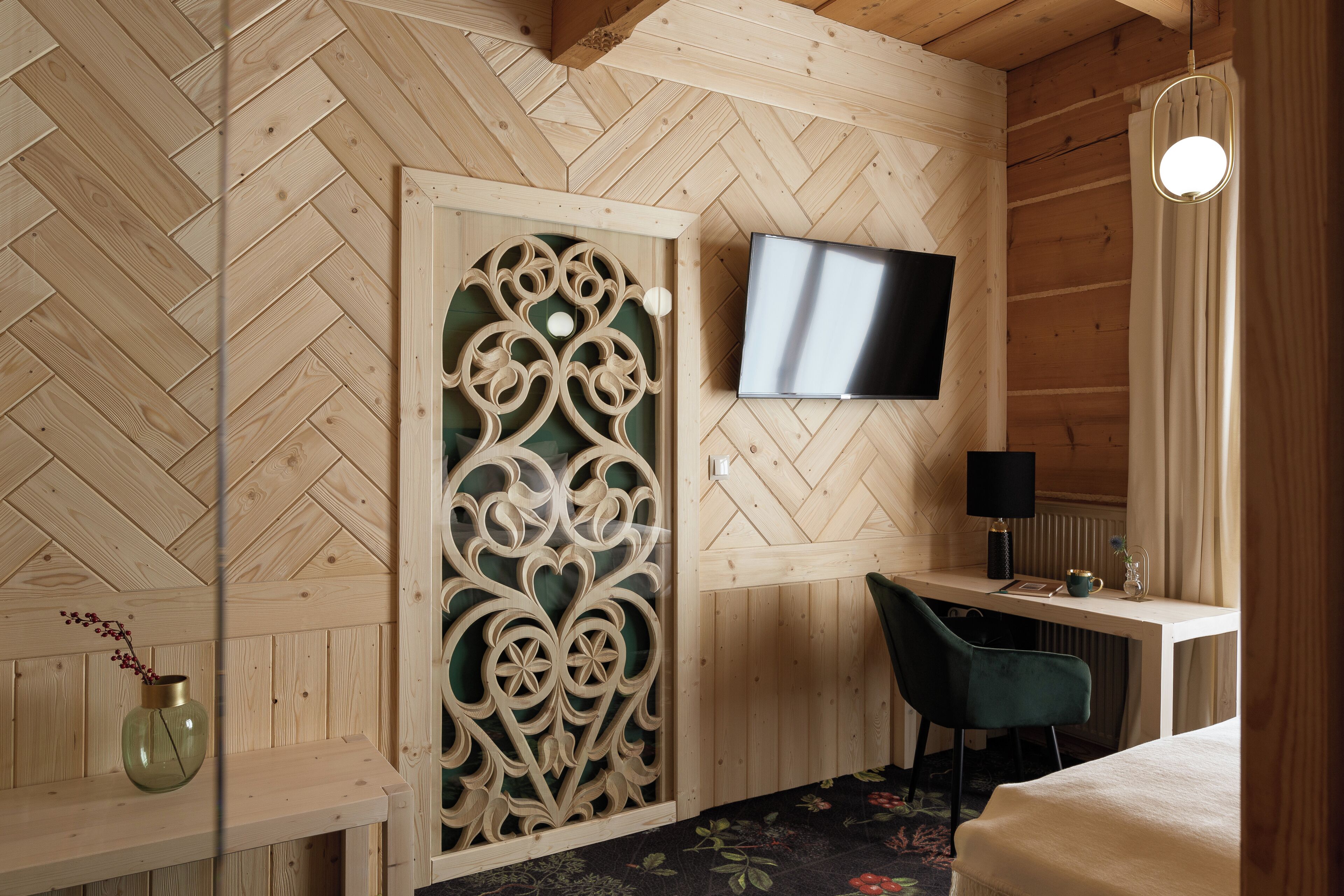 Un intérieur en bois avec un téléviseur fixé au mur, un bureau avec une chaise et une cloison décorative en bois.