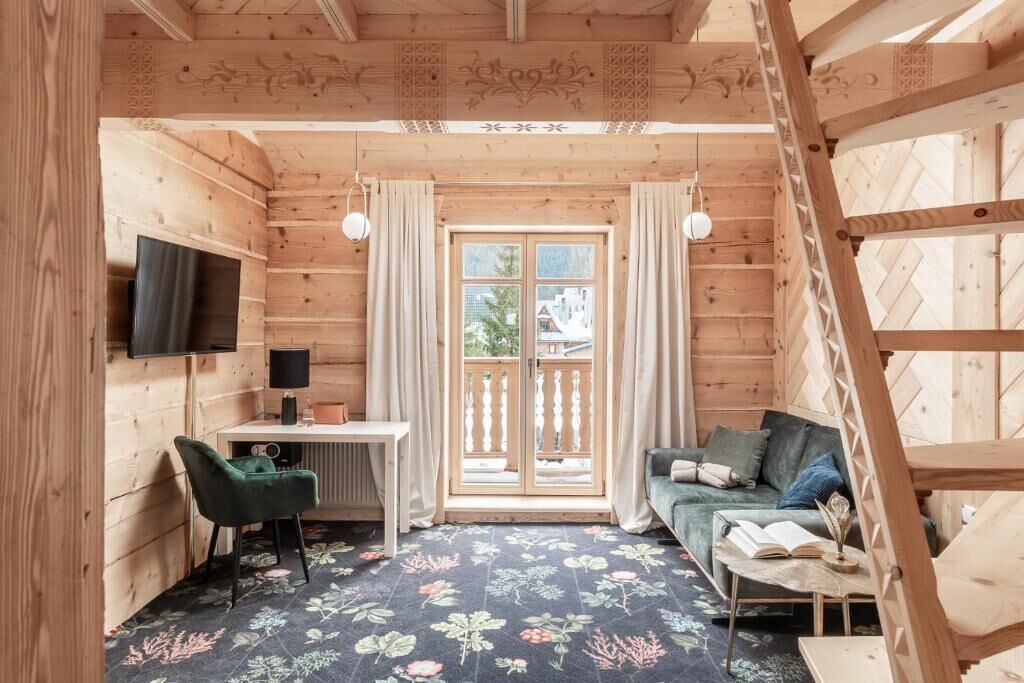A wooden cabin interior with a desk, a sofa, a TV, and a balcony.