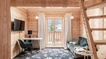 A wooden cabin interior with a desk, a sofa, a TV, and a balcony.
