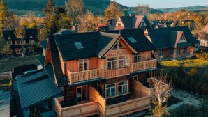 Una casa de madera de varios pisos con un balcón, rodeada de un paisaje boscoso.