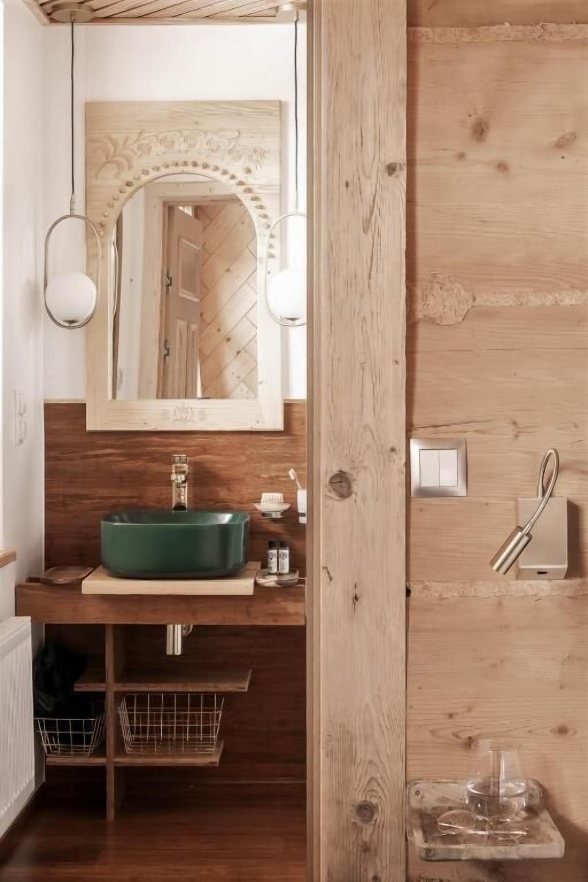 A wooden bathroom with a green sink, a mirror with an ornate frame, and a towel rack.