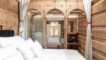 A wooden cabin-style room with a bed, curtains, and a glass door leading to a bathroom.