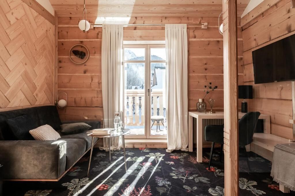A cozy room with a sofa, a small table, a chair, a TV, and a window with curtains.
