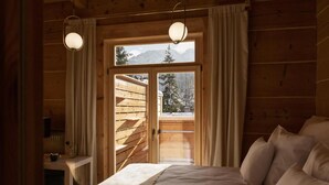 Habitación tipo cabaña de madera con una cama, un escritorio y vistas a las montañas a través de una puerta de cristal.