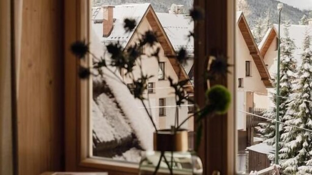 Una ventana con vistas a casas cubiertas de nieve y montañas.