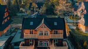 Una casa grande de madera con balcón, rodeada de árboles y un paisaje montañoso.
