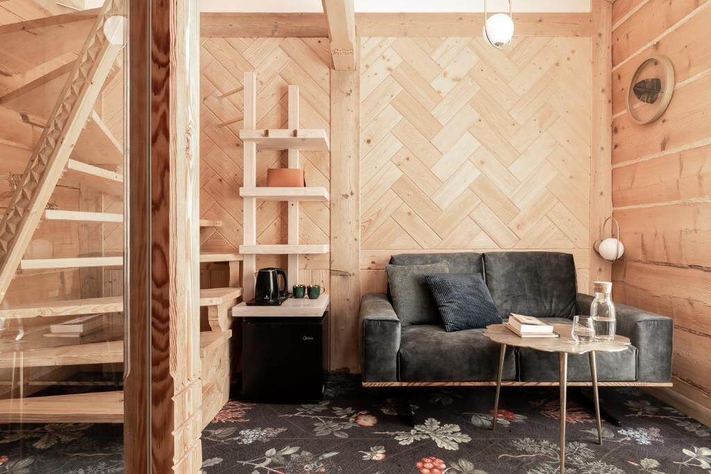 Una habitación acogedora con una pared de madera con patrón de espiga, un sofá, una mesita y una escalera.
