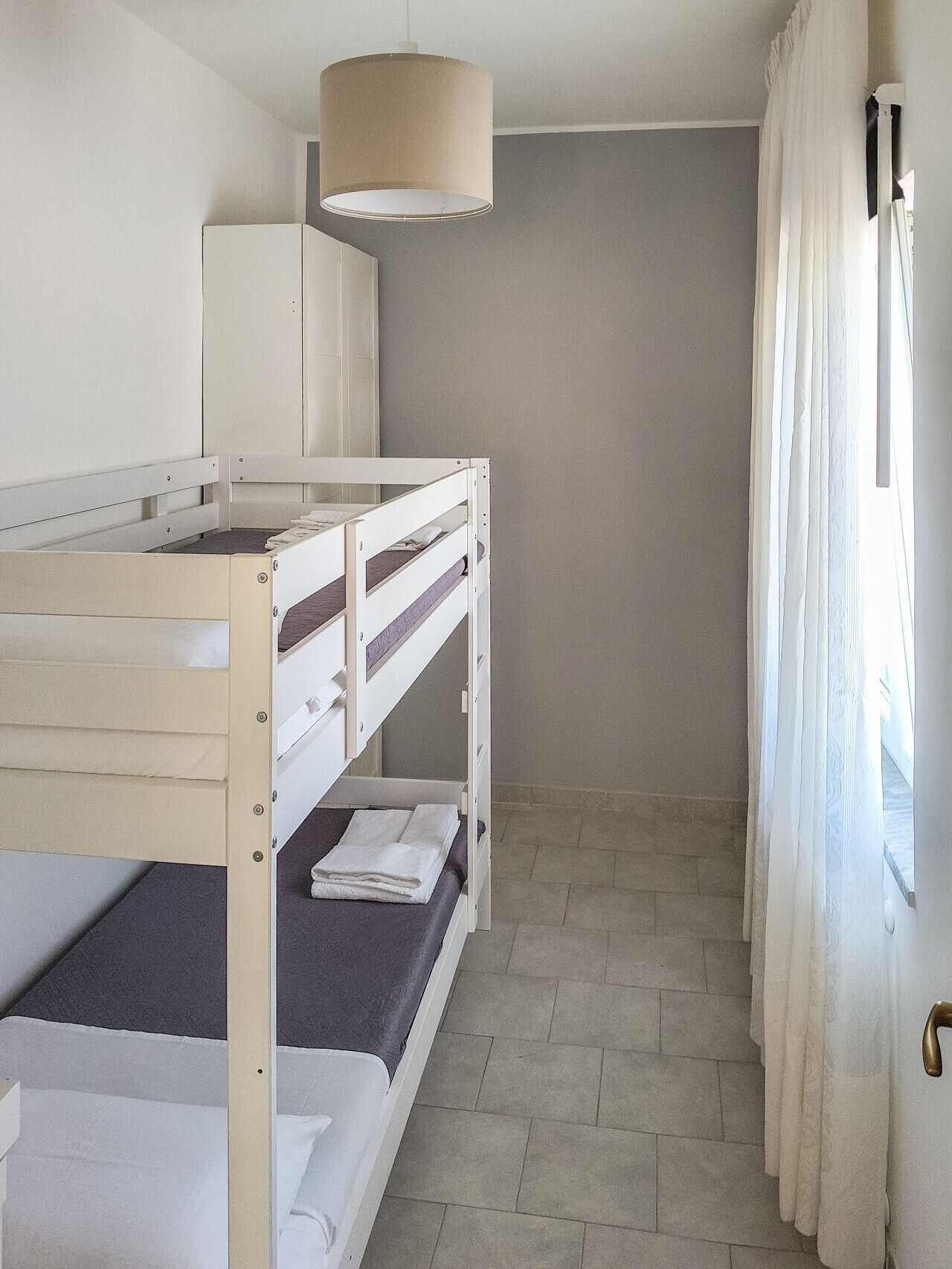 A bunk bed room with a ceiling lamp, a wardrobe, and a window with curtains.